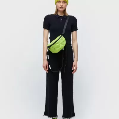 Mulher com roupa preta e acessórios verdes lima, incluindo boné, bolsa e ténis.