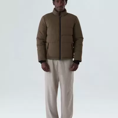 Casaco acolchoado castanho com fecho zip usado por modelo masculino com calças bege