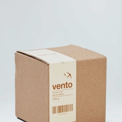 Caixa de cartão com etiqueta branca e texto em castanho indicando vela aromática vento e peso