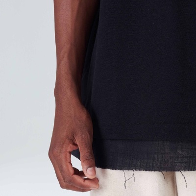 Braço e mão de pessoa com camiseta preta e calças claras com fios soltos