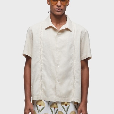 Homem com camisa creme de manga curta e calções floridos com óculos de sol amarelos