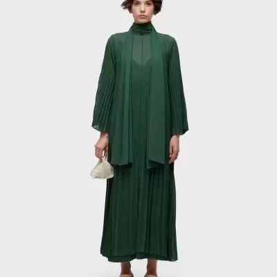 Modelo a usar vestido longo verde escuro com mala branca e sandálias bege.