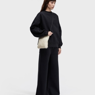 Pessoa com conjunto preto largo, sandálias de pelo branco, mala pequena de pelo branco com alça preta