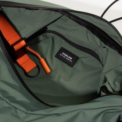 Interior de mochila verde com bolso e etiqueta OSKLEN RIO DE JANEIRO