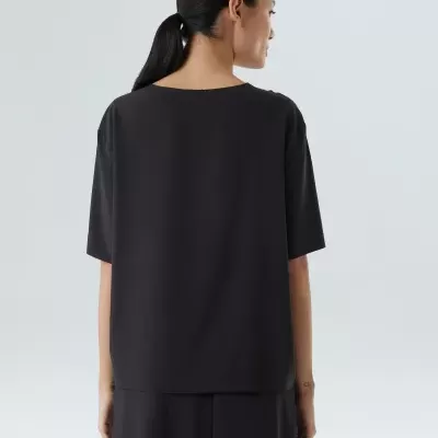 Pessoa de costas com camisola e calças pretas em fundo cinzento claro