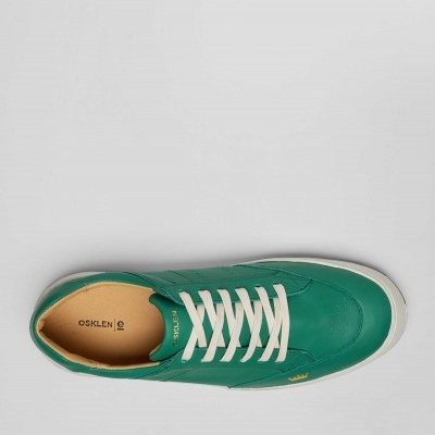 Ténis verde com atacadores brancos sobre fundo cinzento claro