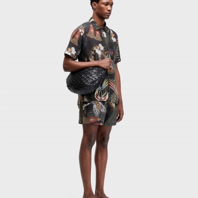 Homem com roupa floral e bolsa preta com textura de escamas