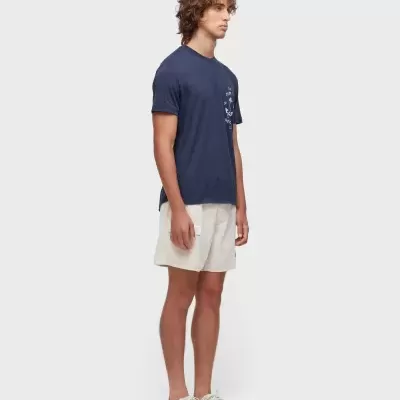 Homem com t-shirt azul escura, calções bege e sapatos brancos em fundo branco