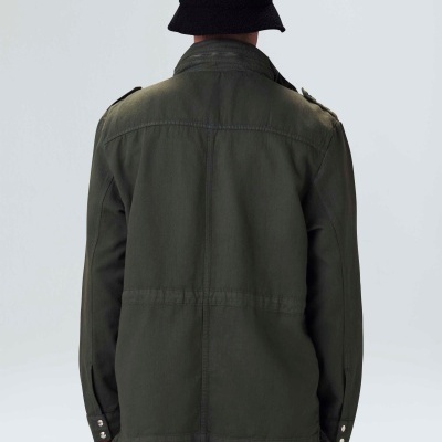 Casaco verde-oliva com chapéu preto em fundo neutro