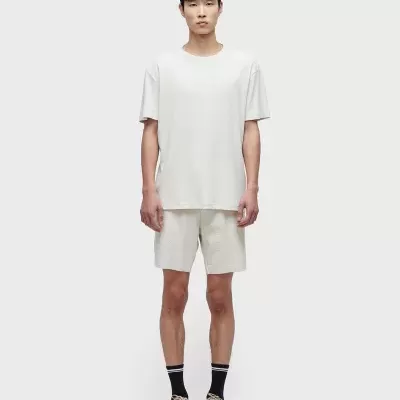 Homem com roupa casual bege com t-shirt e calções.