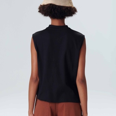 Pessoa de costas com chapéu bege, camisola preta sem mangas e calças castanhas