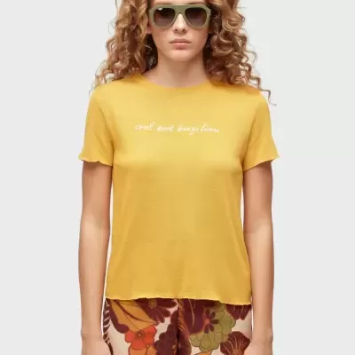 Mulher a usar t-shirt amarela com texto branco e calções florais coloridos.