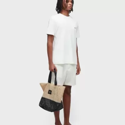 Homem com roupa branca e mala de rede bege e preta em fundo cinza claro