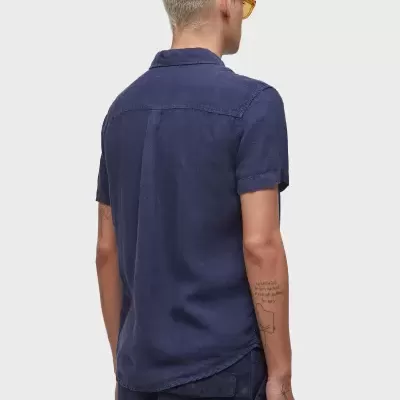 Homem de costas a usar camisa azul escura de manga curta e óculos amarelos