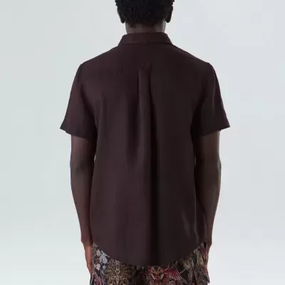 Homem de costas com camisa castanho escuro e calções florais coloridos