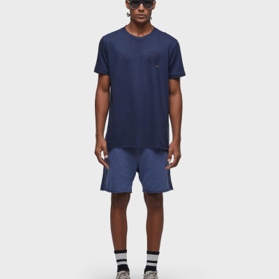 Homem com roupa casual azul e óculos pretos num fundo branco.