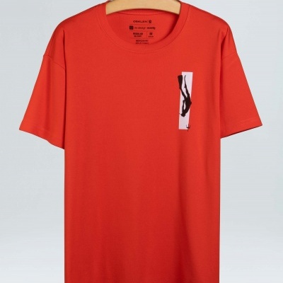 T-shirt vermelha de manga curta com gráfico preto e branco no peito pendurada num cabide de madeira.