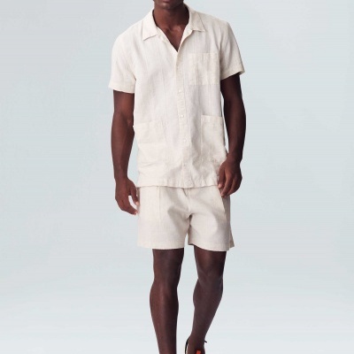 Homem com conjunto bege claro, boné e sapatilhas em fundo claro.