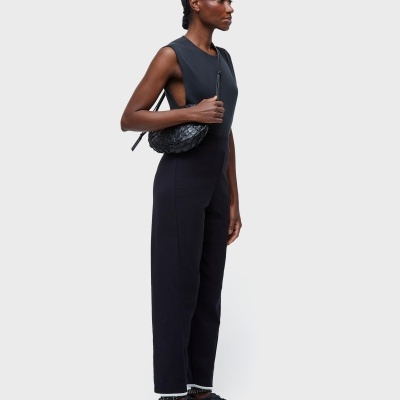 Mulher com macacão preto, mala preta de textura enrugada e sapatos desportivos pretos