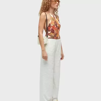 Mulher com macacão estampado e branco, sandálias douradas, bolsa branca e óculos de sol laranja