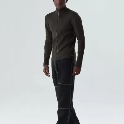 Homem com casaco castanho e calças pretas em fundo claro