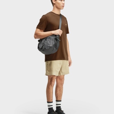 Homem com t-shirt castanha, calções bege e bolsa cinzenta com padrão quadriculado