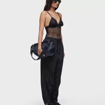 Mulher com roupa preta e bolsa preta em fundo branco