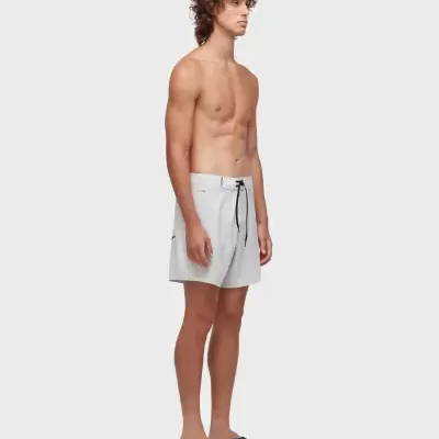 Homem em pé com fato de banho cinzento claro e chinelos pretos