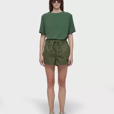 Mulher com t-shirt verde escura, calções verde oliva, tênis bege e óculos de sol