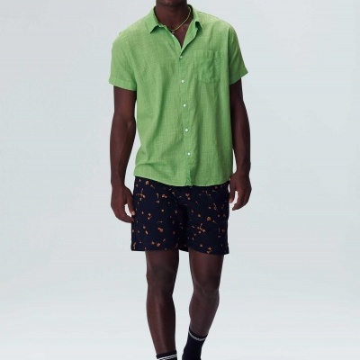 Homem com camisa verde de manga curta e calções pretos com padrão laranja, fundo branco