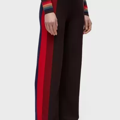 Calças largas pretas com faixas laterais coloridas, camisola de riscas coloridas e sapatilhas brancas