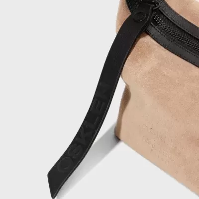 Bolsa bege de camurça com fecho e puxador preto com texto OSKLEN