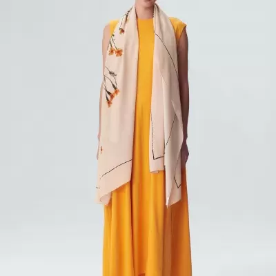 Mulher com vestido amarelo longo, lenço bege com padrão floral e sandálias pretas