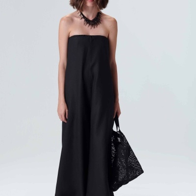 Mulher com macacão preto sem alças e bolsa preta vazada, fundo branco.