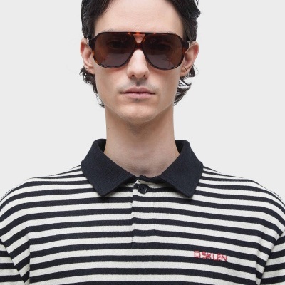 Homem com óculos de sol castanhos e camisa polo riscada preta e branca