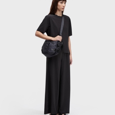 Mulher com roupa preta e bolsa preta com texto OSKLEN