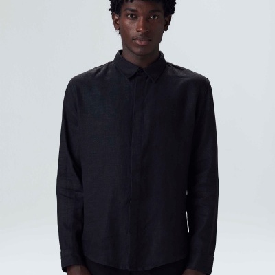 Homem com camisa preta de manga comprida e calças pretas sobre fundo neutro cinzento