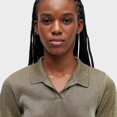 Camisa polo dourada metálica com gola e mangas curtas vista frontalmente em modelo com cabelo trançado
