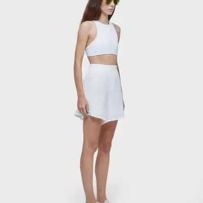 Mulher com top cropped branco, saia curta branca e óculos de sol amarelos