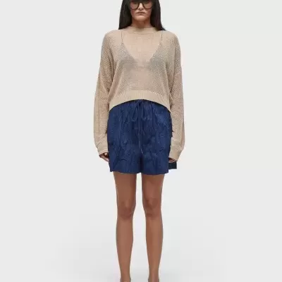 Mulher com camisola de malha bege e calções azul-escuro em fundo branco