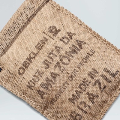 Saco de juta com texto impresso e alça preta sobre fundo cinza