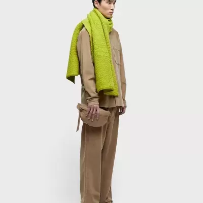 Homem com roupa bege e cachecol verde sobre fundo branco