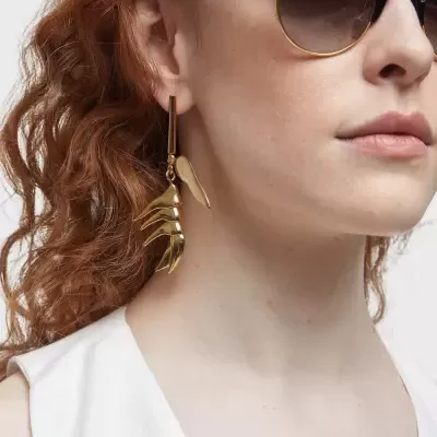 Mulher com óculos de sol pretos e brinco dourado pendente em forma de folha