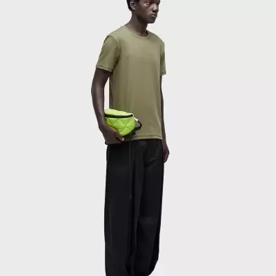 Homem com camiseta verde-oliva, calças pretas, segurando bolsa verde neon acolchoada