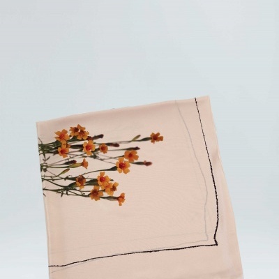 Lenço de tecido bege com flores laranjas e amarelas e linhas pretas na borda