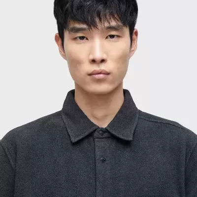 Homem a usar casaco cinzento escuro com botões e bolsos no peito.