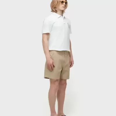 Homem de roupa casual com camisa polo branca e calções bege, sandálias pretas