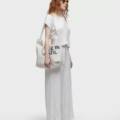 Mulher com roupa branca, óculos amarelos e saco branco com texto