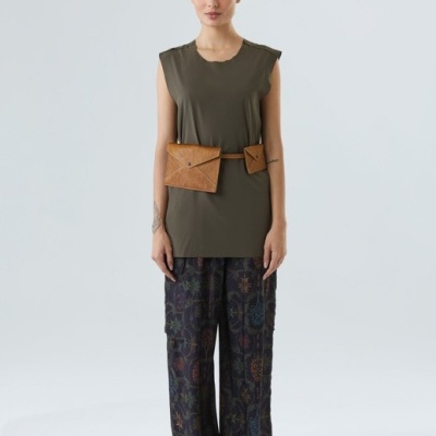 Mulher com blusa verde-oliva, calças estampadas largas, cinto castanho com bolso e sapatos pretos