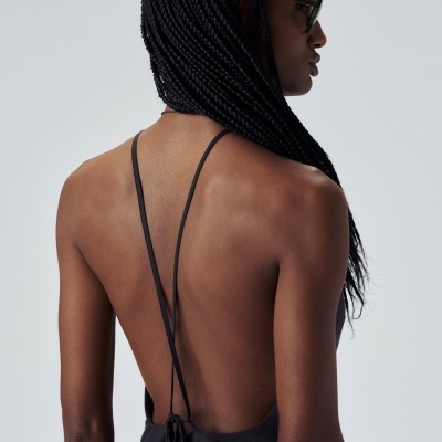 Mulher de costas com vestido preto de alças finas cruzadas e cabelo em tranças.